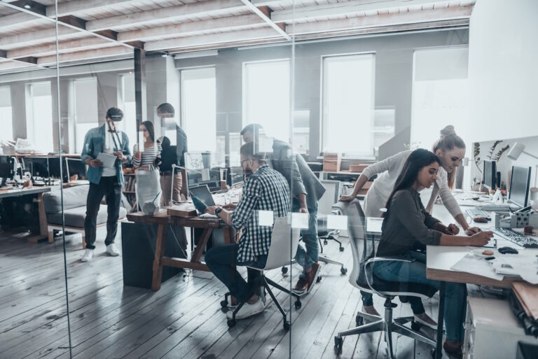 Fiatal csapat open office irodában közösen dolgozik számítógépeken