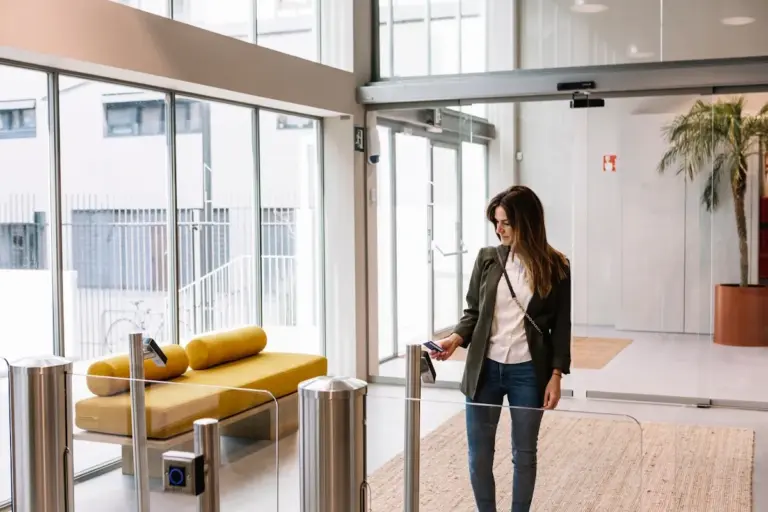 Beléptetőkapun áthaladó nő modern irodaház recepciós terében, amely a vendégfogadás és hozzáférési szabályok szerepét mutatja be.